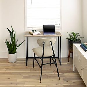 Minimalist home office setup with a wooden desk, laptop, chair, two plants, and a book under a bright window.