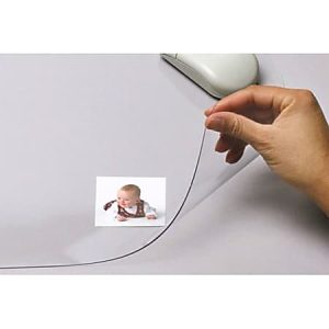 Hand lifting a transparent desk pad to reveal a photo of a baby underneath, with a computer mouse nearby.