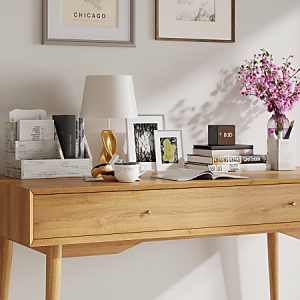 Wooden desk with books, a lamp, pink flowers, and decor in a bright room. Framed pictures and art on the wall above.