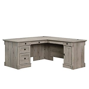 L-shaped wooden desk with a distressed light gray finish, featuring multiple drawers and a cabinet for storage.