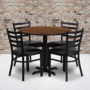 Round wooden table with four black chairs against a brick wall background on a light floor.